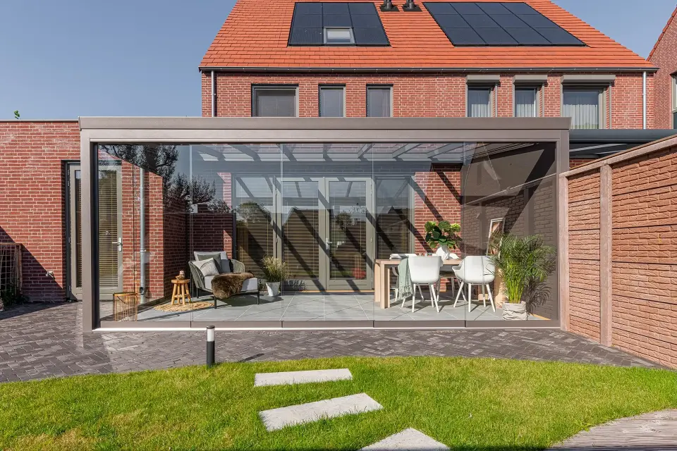 Moderner Wintergarten mit Glasw&auml;nden und Aluminiumrahmen, stilvoll eingerichtet mit Sitz- und Essbereich.